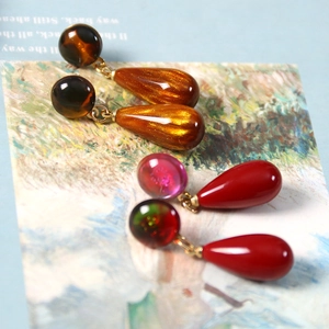 Macro detail of amber and red teardrop resin earrings displayed on a text card