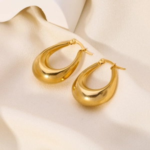 Detail view of high-polished gold teardrop earrings on elegant beige silk fabric