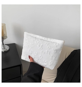 Close-up of a white fabric clutch bag with embossed floral patterns held by hand