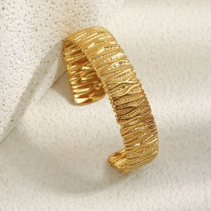 Gros plan sur un bracelet manchette doré avec motifs ondulés verticaux irréguliers