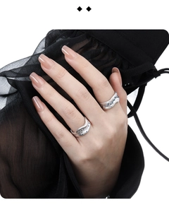 Detail showing irregular textured silver rings with small blue gemstones worn on hand