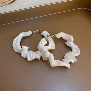 Detail view of white pleated satin hoop earrings on a vintage bronze jewelry tray