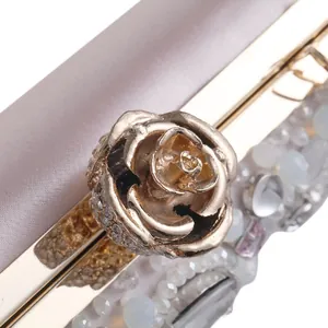 Dettaglio della chiusura a rosa dorata con diamanti e perle su borsa da sera in raso champagne