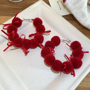 Detail view of red velvet pompom and silk bow earrings with elegant silver needles