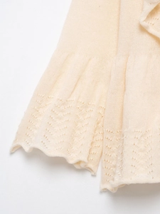 Detail of pointelle knit pattern and ruffled hem on a creamy white knit sweater