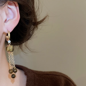 Close-up of gold tassel earrings with brown tiger eye beads on model for luxury look