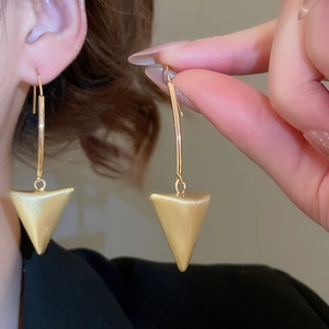 Macro view of minimalist 18k gold matte brushed metal triangle dangle earrings on model