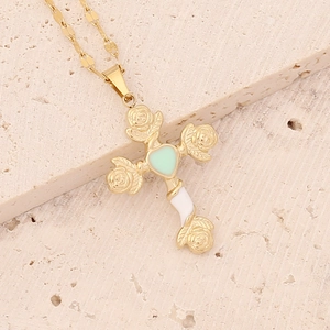 Close-up of gold cross pendant with rose texture and green heart on beige stone