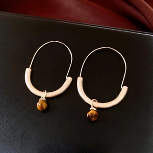 Macro detail of golden hoop earrings featuring polished tiger's eye stone bead pendants