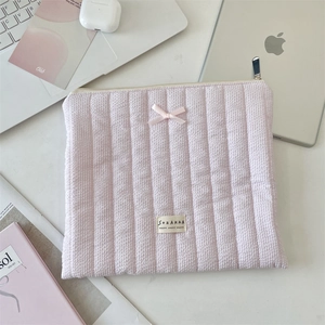 Detailed view of pink quilted laptop sleeve with soft ribbon bow and organized desk items