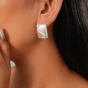 Close-up of matte silver rectangular earring with S-shaped zircon inlay on a model