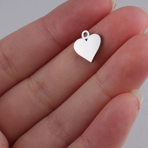 Macro shot of a tiny silver heart pendant on a finger to show the small scale and detail