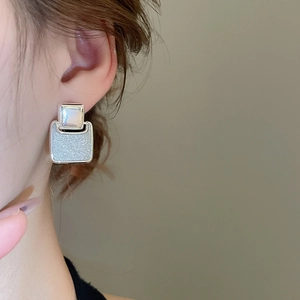 Close-up of 18k gold plated square stud earrings with starburst shimmer on model ear