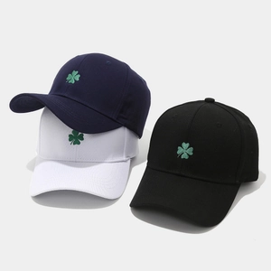 Three embroidered shamrock baseball caps in navy, white, and black on a grey background