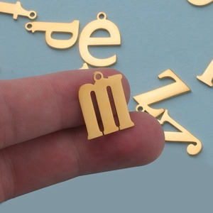 Close-up of golden stainless steel letter M pendant held by hand for jewelry making