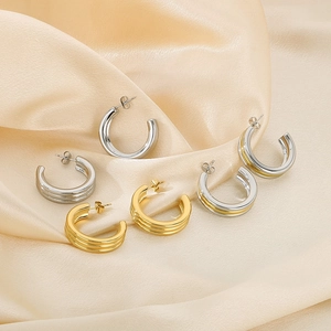 Detailed view of gold and silver C-shaped stainless steel earrings on silk background