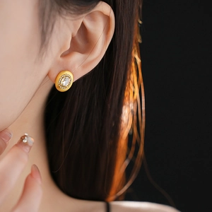 Close-up of elegant gold oval stud earring with central stone and crystal halo on ear