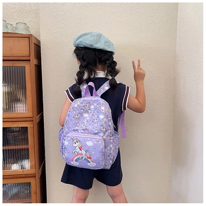 Rear view of a child wearing the purple unicorn and rainbow print backpack in a room