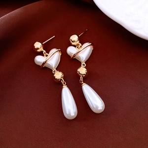 Detailed view of vintage pearl heart drop earrings with gold finish on dark fabric