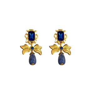 Elegant gold bow earrings with square blue rhinestones and teardrop pendants on white background