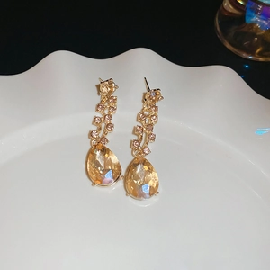 Macro detail of teardrop earrings with champagne crystals on a white ceramic plate