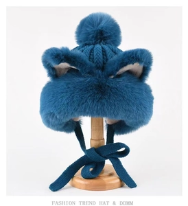 Close-up of dark blue faux fur hat with cat ears and matching pom-poms on a wooden stand