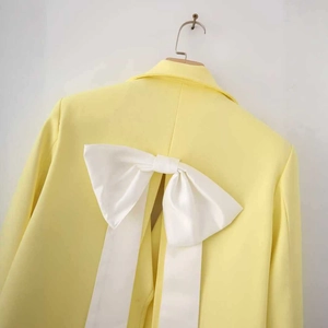 Back view of a yellow satin blazer for women featuring a large white bow and back slit detail