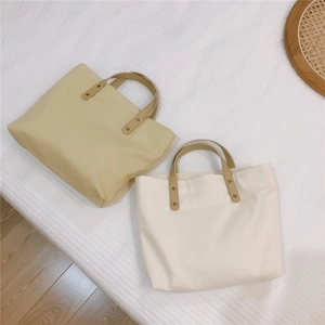 Close-up of canvas handbags with brown leather handles and reinforced metal rivets