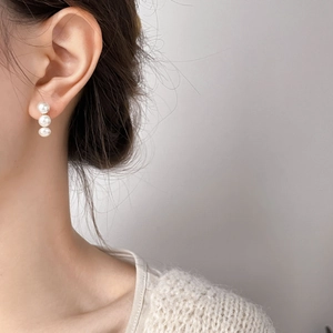Elegant triple white pearl drop earrings with gold base shown on a model in knitwear