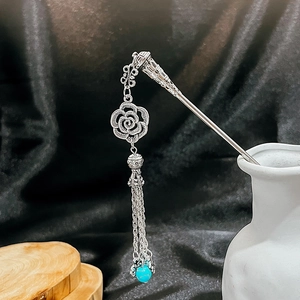 Detail of silver rose hair pin with turquoise beads and metallic tassels on a vase