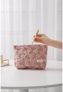 Detail of hand putting a gold beauty tool into a pink corduroy lace floral cosmetic bag