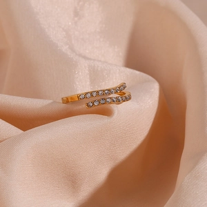Detail of adjustable gold-plated cross ring with clear zircons on pink satin fabric