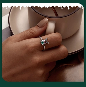 Close-up of reindeer ring with green and pink stones worn by model in cozy setting