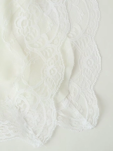Close-up of white floral lace fabric with delicate embroidery and scalloped edges