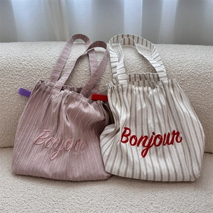 Detail view of striped canvas tote bags with Bonjour embroidery and drawstring closure