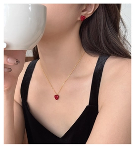 Close-up of elegant gold necklace and stud earrings set with small red heart pendants