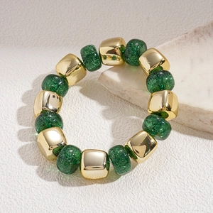 Close-up of green glazed glass beads and golden metal cubes on a minimalist stone base