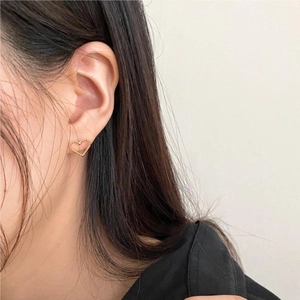 Close-up of golden hollow heart earrings with twisted rope texture on a model's ear