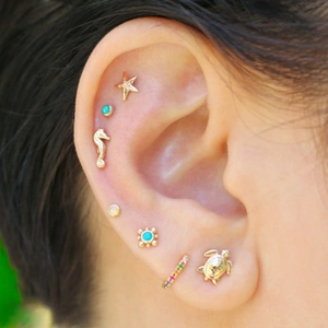 Close-up of golden turtle, starfish, and seahorse turquoise piercing studs on model ear