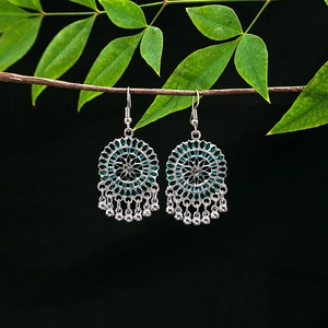 Detail of silver drop earrings with green floral patterns and metal bead tassels on a branch