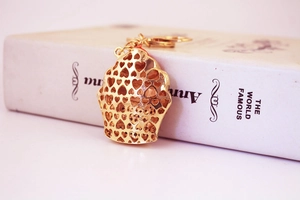 Detailed view of golden cupcake keychain with hollow heart patterns on a white book