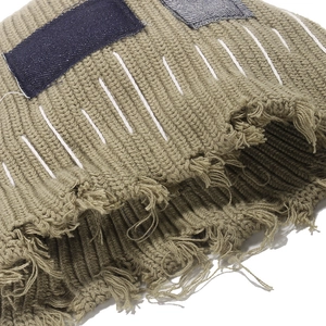 Detailed texture of olive knit hat with distressed denim patches and frayed edges