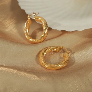Elegant gold twisted hoop earrings placed on luxury champagne silk and white seashell