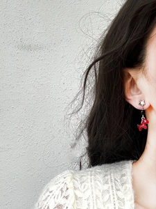 Close-up of a silver star stud earring featuring a cute red horse pendant on a model