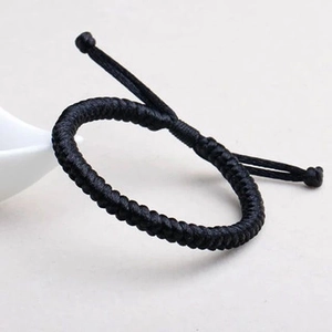 Macro shot of a black hand-woven bracelet with adjustable cord on a gray background