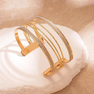 Detailed close-up of a layered gold and silver glitter cuff bracelet on a white stone