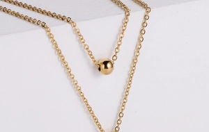 Close-up of a double-layered gold titanium steel necklace with a polished sphere pendant