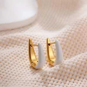Detail shot of U-shaped gold earrings with white enamel on a beige textured fabric background