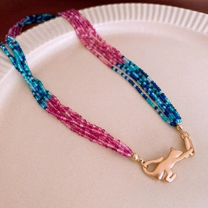 Detail of multi-strand beaded necklace with a golden cat clasp on white ceramic tray