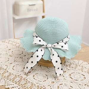 Close-up of mint green straw hat with white polka dot bow and lace trim on brim